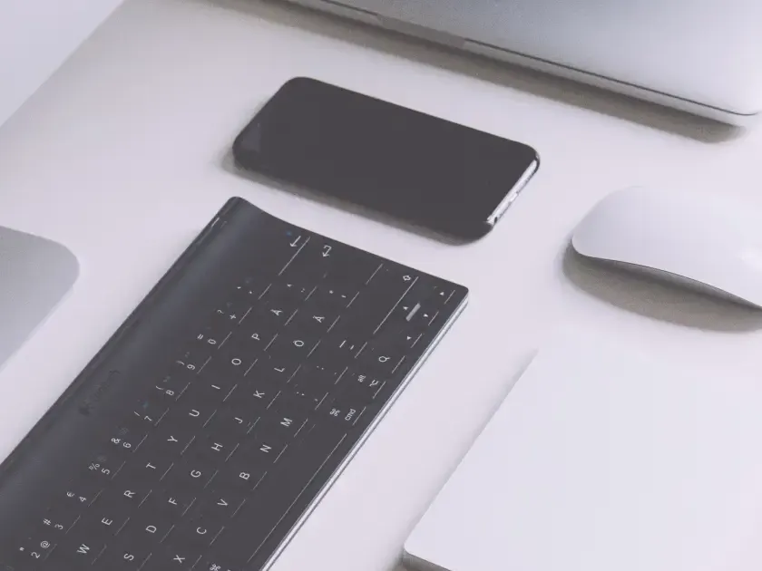 Smartphone auf einem Schreibtisch neben Tastatur und Maus